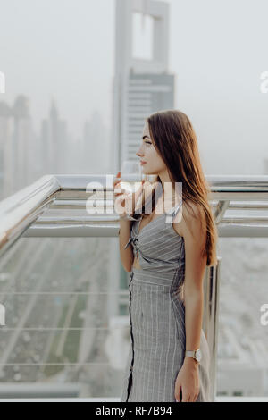 Jeune femme verre vin blanc sur la terrasse du restaurant et profiter de la vue panoramique sur le centre-ville de Dubaï l'architecture. Banque D'Images