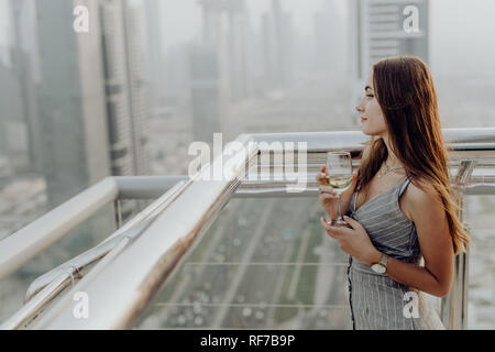 Jeune femme verre vin blanc sur la terrasse du restaurant et profiter de la vue panoramique sur le centre-ville de Dubaï l'architecture. Banque D'Images