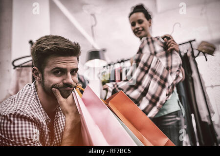 Bored man with shopping bags tout en femme par porte manteau Banque D'Images