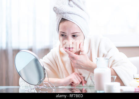 Belle jeune femme malheureuse avec une serviette sur la tête détecte l'acné sur son visage. Concept d'hygiène et de soins pour la peau Banque D'Images