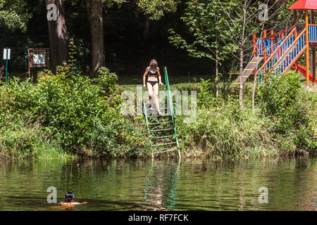 Une femme d'âge moyen en bikini descend les escaliers dans la rivière Otava, Bohême du Sud, vacances d'été en République tchèque Banque D'Images