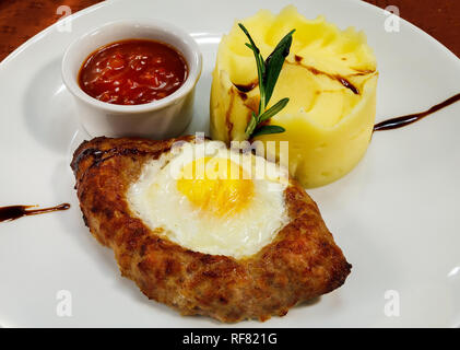 Patty cuit en forme de bateau avec oeuf sur le haut, purée de pommes de terre et sauce tomate épicée sur une plaque blanche Banque D'Images