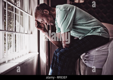 Vue latérale d'une senior man sitting on bed by window Banque D'Images
