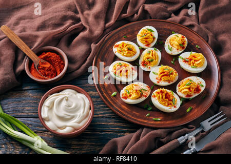 Oeufs farcis saupoudré de paprika et de l'oignon vert haché finement sur une plaque de faïence sur une vieille table en bois rustique avec tissu brun, vue d'un Banque D'Images