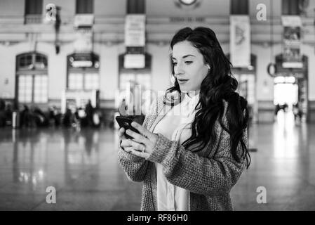 Belle femme mature contrôler les horaires de train sur son téléphone mobile, photo en blanck et blanc. Banque D'Images