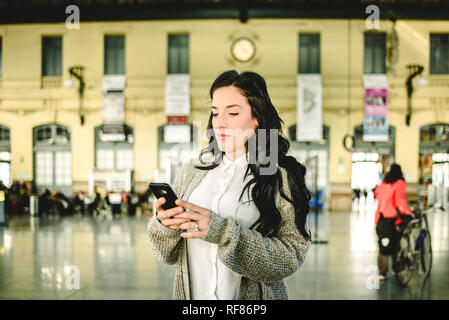 Belle femme mature contrôler les horaires de son train sur son téléphone mobile. Banque D'Images