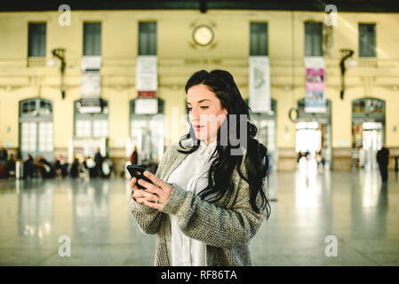 Belle femme mature contrôler les horaires de son train sur son téléphone mobile. Banque D'Images