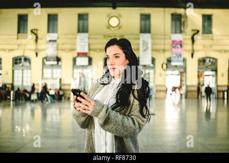 Belle femme mature contrôler les horaires de train sur son mobile son phonelooking à l'avant Banque D'Images