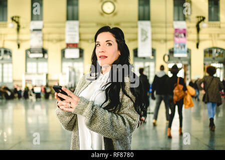 Belle femme mature contrôler les horaires de son train sur son téléphone mobile. Banque D'Images