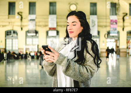 Belle femme mature contrôler les horaires de son train sur son téléphone mobile. Banque D'Images