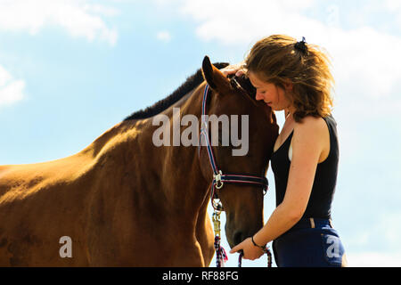 Prendre soin des animaux, l'amour et l'amitié concept. Jeune fille Jockey cheval brun embrasser et s'étreindre sur sunny day Banque D'Images