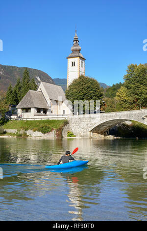 L'église de St Jean le Baptiste, Cerkev Sv. Janeza Krstnika, et le lac de Bohinj, Bohinj, Ribcev Laz, Haute-Carniole, la Slovénie. Avec les canoéistes sur le lac Banque D'Images