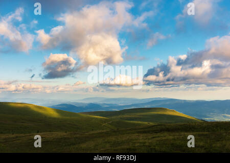 Soirée magnifique paysage. Superbe vue depuis la colline herbeuse dans à la vallée éloignée et crête de montagne. fluffy clouds sur le ciel paisible Idyll. Banque D'Images