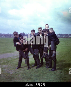 1962, historique, groupe de jeunes écoliers en uniforme britannique, de s'amuser ensemble dans un champ ou un parc par leur école, Liverpool, Angleterre, Royaume-Uni, avec deux des garçons sur piggyback. Banque D'Images