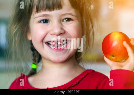 Une jolie petite fille de papier frisé sourit et est titulaire d'une pomme rouge. Portrait d'un bébé heureux de manger une pomme rouge. L'enfant perd des dents de lait. L'alimentation saine Banque D'Images