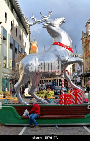 Un jeune homme assis sous un géant de l'alimentation des rennes d'argent Décorées pour Noël dans jardin du couvent Central London England UK Banque D'Images