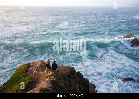 Un jeune couple qui regarde les vagues puissantes s'écraser sur le rivage. Banque D'Images