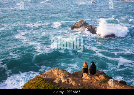 Un jeune couple qui regarde les vagues puissantes s'écraser sur le rivage. Banque D'Images