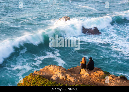 Un jeune couple qui regarde les vagues puissantes s'écraser sur le rivage. Banque D'Images