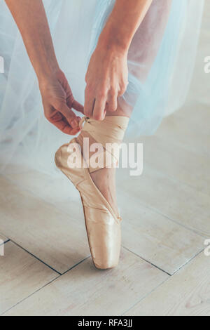 Mains de ballerine en tutu bleu jupe met sur les pointes sur une jambe dans la lumière blanche hall. Jeune femme danseuse de ballet classique en classe de danse Banque D'Images