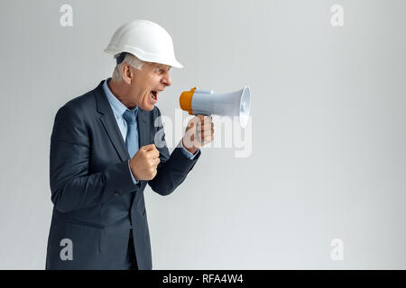 L'occupation professionnelle. Constructeur dans hard hat isolés sur gris criant à l'orateur en colère faisant fist Banque D'Images