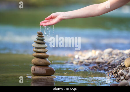 Close-up résumé image de femme part verser de l'eau sur les différentes tailles inégales brun naturel et la forme des pierres comme équilibrée pile pyramide monument Banque D'Images