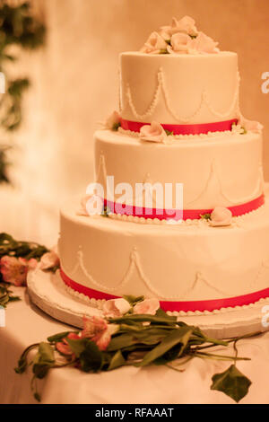 Gâteau de mariage à l'écran aux côtés de fleurs, sur une table, au cours d'une réception de mariage. Banque D'Images