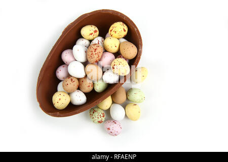 Mini oeufs de Pâques en chocolat dans la moitié d'un gros œuf en chocolat panier sur un fond blanc. Banque D'Images