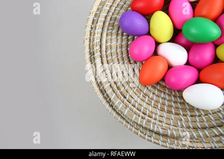 Les oeufs de Pâques colorés, dans un panier de paille sur un arrière-plan gris. Banque D'Images
