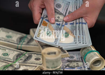 Femme tenant une poignée de billets de 100 USD en éventail sur des piles de l'argent sur une table d'un versement , business, le succès ou la corruption concept dans un proche u Banque D'Images