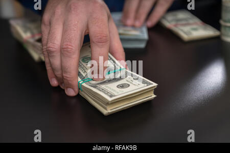 L'homme placé un pari, effectuer le paiement ou l'offre d'un pot-au-dessus d'une grande pile de 100 dollar bills dans une vue en gros plan sur sa main Banque D'Images