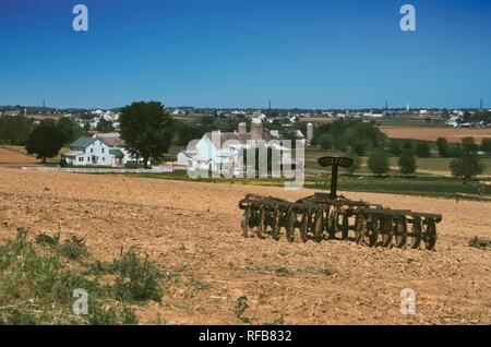 Amish Farm Avec Vintage Old Rusty Farm Equipment mise sur le terrain avec grange et maison de ferme sur une journée ensoleillée Banque D'Images