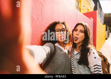 Heureux les jeunes filles s'amuser en plein air et prendre. selfies Heureux amis féminins montrant leur langue maternelle de couleur après avoir mangé un bonbon. Banque D'Images