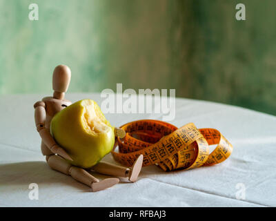 Une figurine en bois avec un mordu de pomme verte et d'un ruban de mesure, sur une table Banque D'Images