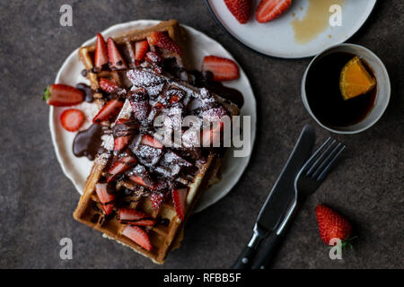 Petit-déjeuner romantique avec gaufres belges avec fraise et chocolat, avec deux tasses de thé au citron, près de fourchette et couteau à fond sombre. Concep Banque D'Images