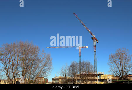 Unfinished building construction and building cranes against clear blue sky background Banque D'Images