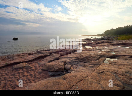 Soirée d'été ensoleillé par la mer. Moulins à vent lointain sur l'arrière-plan. Des rochers et du sable sur la plage. Reposaari, Pori, Finlande. Prise de vue au grand angle. Banque D'Images