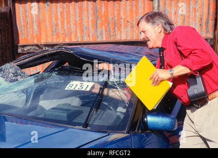 Un expert en sinistres d'assurance inspecte une voiture récemment détruite dans un chantier naval, USA 1993 Banque D'Images