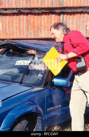 Un expert en sinistres d'assurance inspecte une voiture récemment détruite dans un chantier naval, USA 1993 Banque D'Images