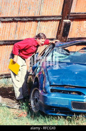 Un expert en sinistres d'assurance inspecte une voiture récemment détruite dans un chantier naval, USA 1993 Banque D'Images