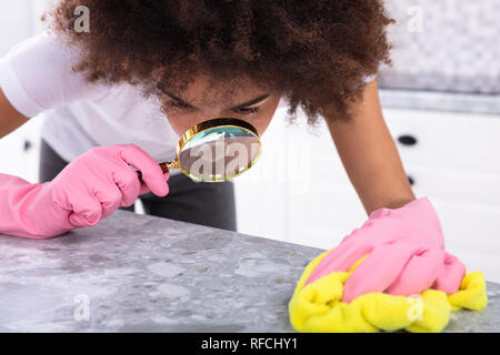 Portrait d'une jeune femme portant des gants rose à la cuisine au comptoir avec loupe Banque D'Images