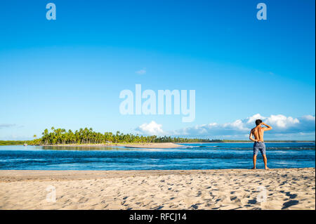 Vue panoramique lumineux d'une plage rustique sur une île au large de la côte de Bahia, au Brésil, avec une figure solitaire à la recherche à l'horizon Banque D'Images