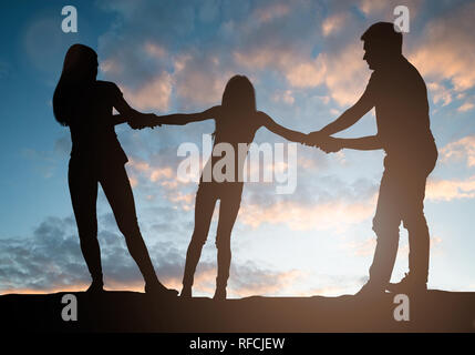 Silhouette de parents tirant leur enfant contre l'autre en face de ciel nuageux Banque D'Images