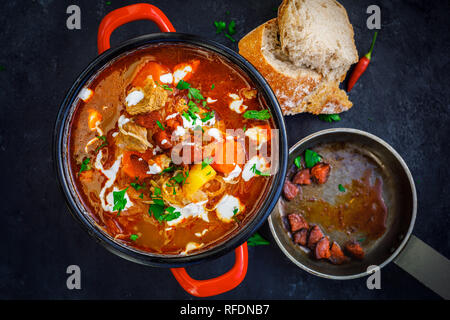 Goulash en pot rouge et les tranches de pain sur le fond du Conseil noir rustique Banque D'Images