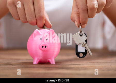 Close-up of a person's Hand Holding Keys Insertion pièce dans la tirelire sur le bureau en bois Banque D'Images