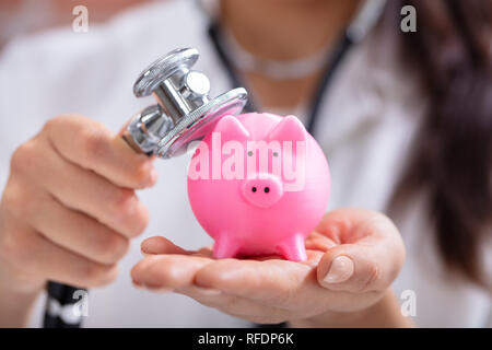 Close-up of main du médecin examinant Pink Piggybank with Stethoscope Banque D'Images