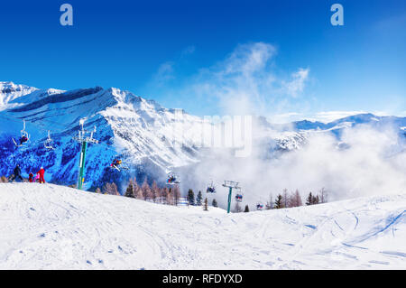 Les skieurs et planchistes non identifiables sur télésiège remontant une pente de ski dans la montagne enneigée (éventail des Rocheuses canadiennes. Banque D'Images