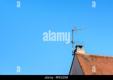 Low angle view of une antenne fixée à la cheminée sur le toit de tuiles d'une maison individuelle contre le ciel bleu. Banque D'Images