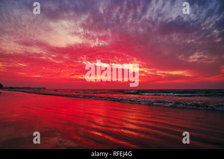 Le lumineux ciel coucher de soleil rouge flamy reflétée dans les vagues d'oscillation de Baie du Bengale sur la plage de Chaung Tha, le Myanmar. Banque D'Images