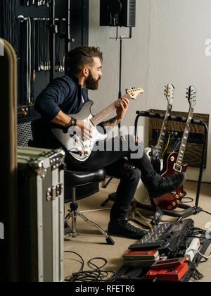 Photo d'un homme à barbe assis et jouant de sa guitare électrique dans un studio d'enregistrement. Banque D'Images